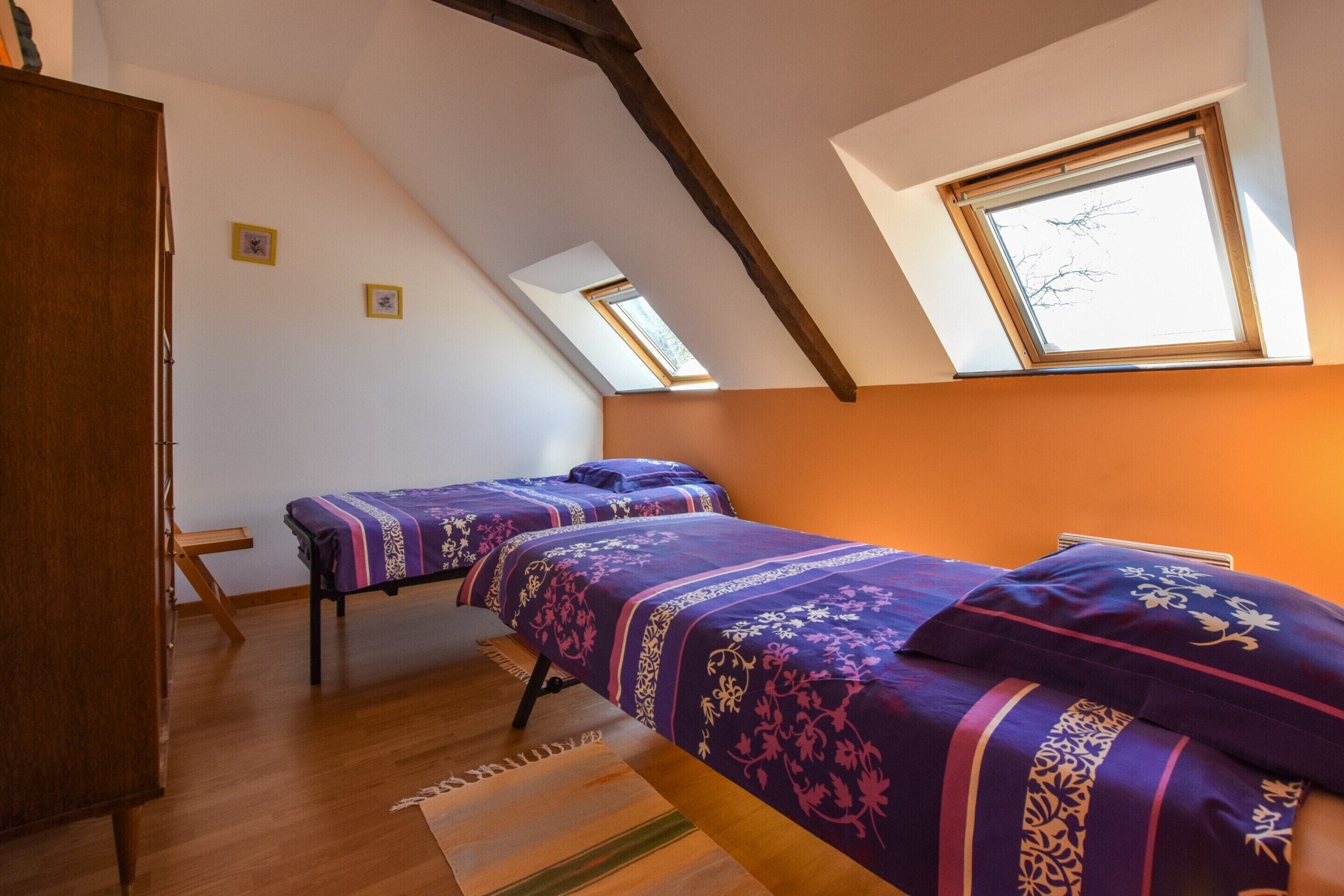 A bedroom with two beds, wooden flooring, a skylight, and a wooden wardrobe.