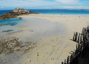 Ein Strand mit einer historischen Festung, klarem blauen Wasser und sandigem Ufer.