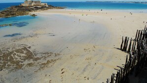Una playa con un fuerte histórico, orilla de arena y mar tranquilo.