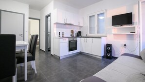 Una cocina moderna con armarios blancos, horno integrado y cafetera. Cuenta con un comedor con mesa y sillas, y un televisor montado sobre la encimera de la cocina.