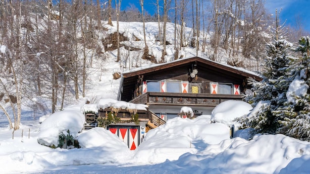 A wooden chalet surrounded by snow-covered trees and a clear blue sky.