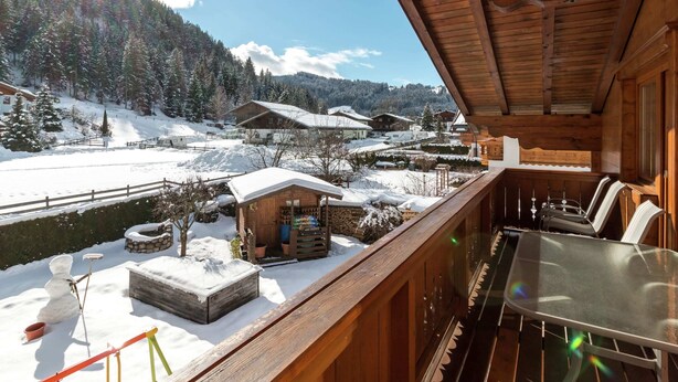 A wooden cabin with a balcony overlooking a snowy landscape, a small outdoor seating area, and a view of neighboring houses and trees. - Apartment Near the ski Area in the Salzburg Region (Altenmarkt im Pongau)