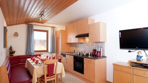 A compact kitchen with wooden cabinets, a dining area with a red bench, and a television on a wooden stand. - Apartment Near the ski Area in the Salzburg Region (Altenmarkt im Pongau)