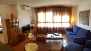 A living room with a blue sofa, a coffee table, a TV, and a dining area with a table and chairs. - Duplex 3-3 La Farola (Manresa)