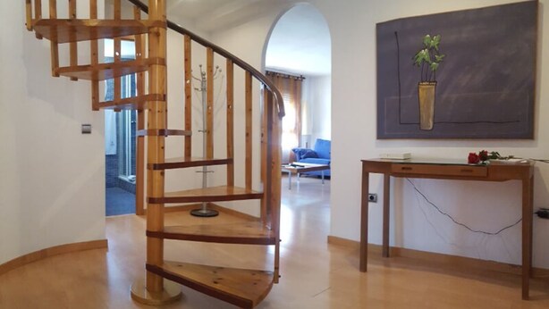 A wooden spiral staircase in a room with a blue sofa and a painting of a plant on the wall. - Duplex 3-3 La Farola (Manresa)