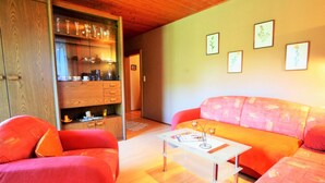 Un soggiorno con soffitto in legno, un tavolino da caffè in vetro, un divano rosso e un mobile in legno con bicchieri.