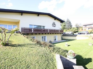 A two-story building with a balcony, a small garden area, and a driveway with parked cars.