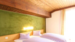 A hotel room with a wooden ceiling, a green accent wall, a bed with striped bedding, a nightstand, and a wall-mounted light. - Spacious Apartment near Ski Area in Mittersill (Mittersill)