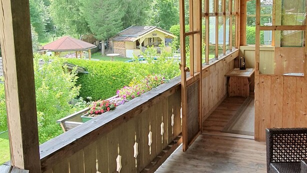 A wooden balcony with a view of a garden and a small house. - Cosy Apartment in Neukirchen near Krimmler Waterfalls (Neukirchen am Grossvenediger)