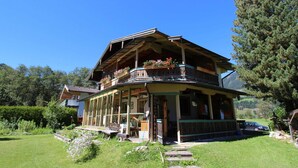 A traditional wooden chalet with a balcony, surrounded by a well-maintained garden and a clear blue sky. - Cosy Apartment in Neukirchen near Krimmler Waterfalls (Neukirchen am Grossvenediger)