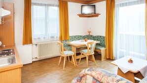 Tunnelmallinen huone, jossa on puinen katto, ruokapöytä tuoleineen, sohva ja televisiotaulutelineellä.