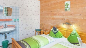 Huoneessa on puinen katto, vihreä- ja valkoisilla tekstiileillä varustettu sänky, puinen yöpöytä, peili sekä kylpyhuone, jossa on pesuallas ja pyyhkeitä.
