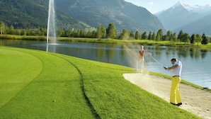 A golf course with a fountain, a lake, and mountains in the background.