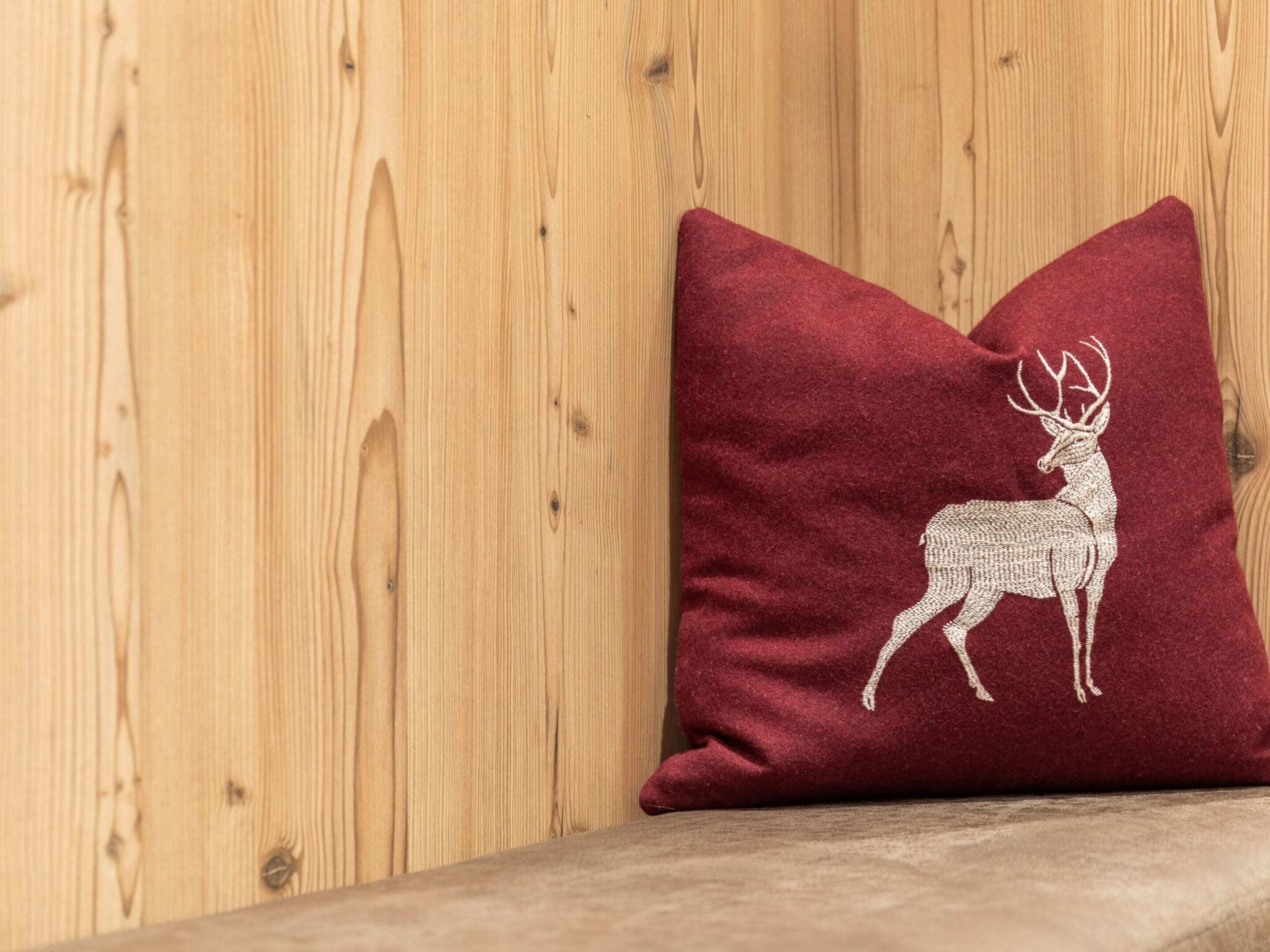A red pillow with a white embroidered deer on a wooden surface.