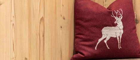 A red pillow with a white embroidered deer on a wooden surface.
