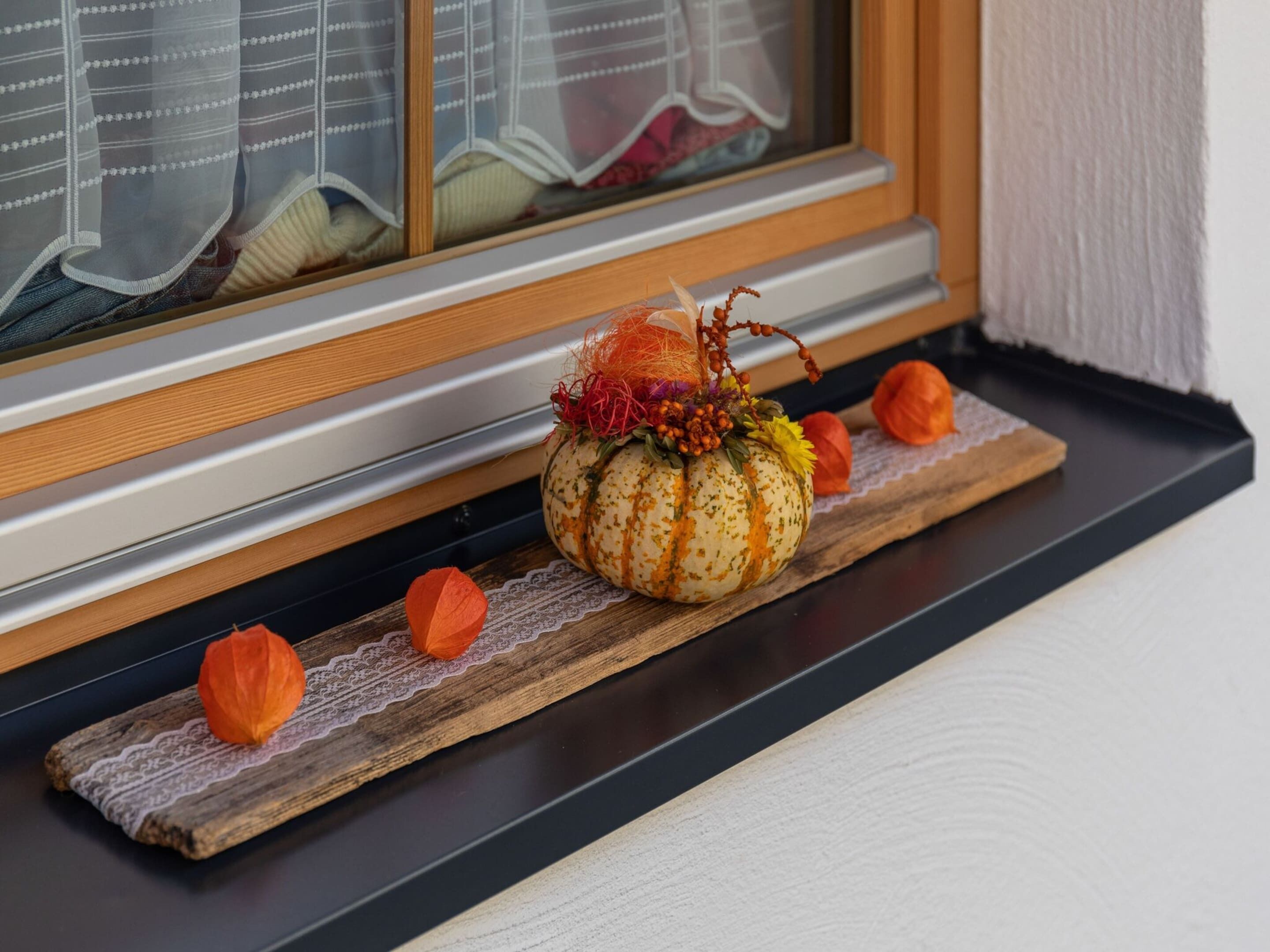 Une composition décorative de citrouilles, présentée sur un plateau en bois près d’une fenêtre ornée de dentelle.