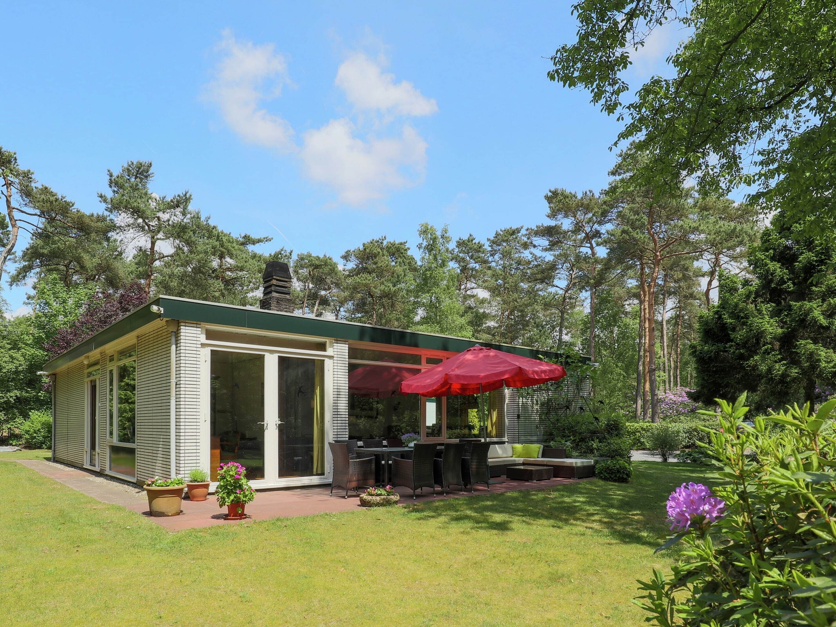 A small, single-story building with a patio area, outdoor seating, and a red umbrella.