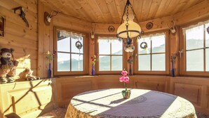 A cozy room with a wooden interior, a round table with a patterned tablecloth, and a view of mountains through large windows. - Chalet on the Slopes (Piesendorf)