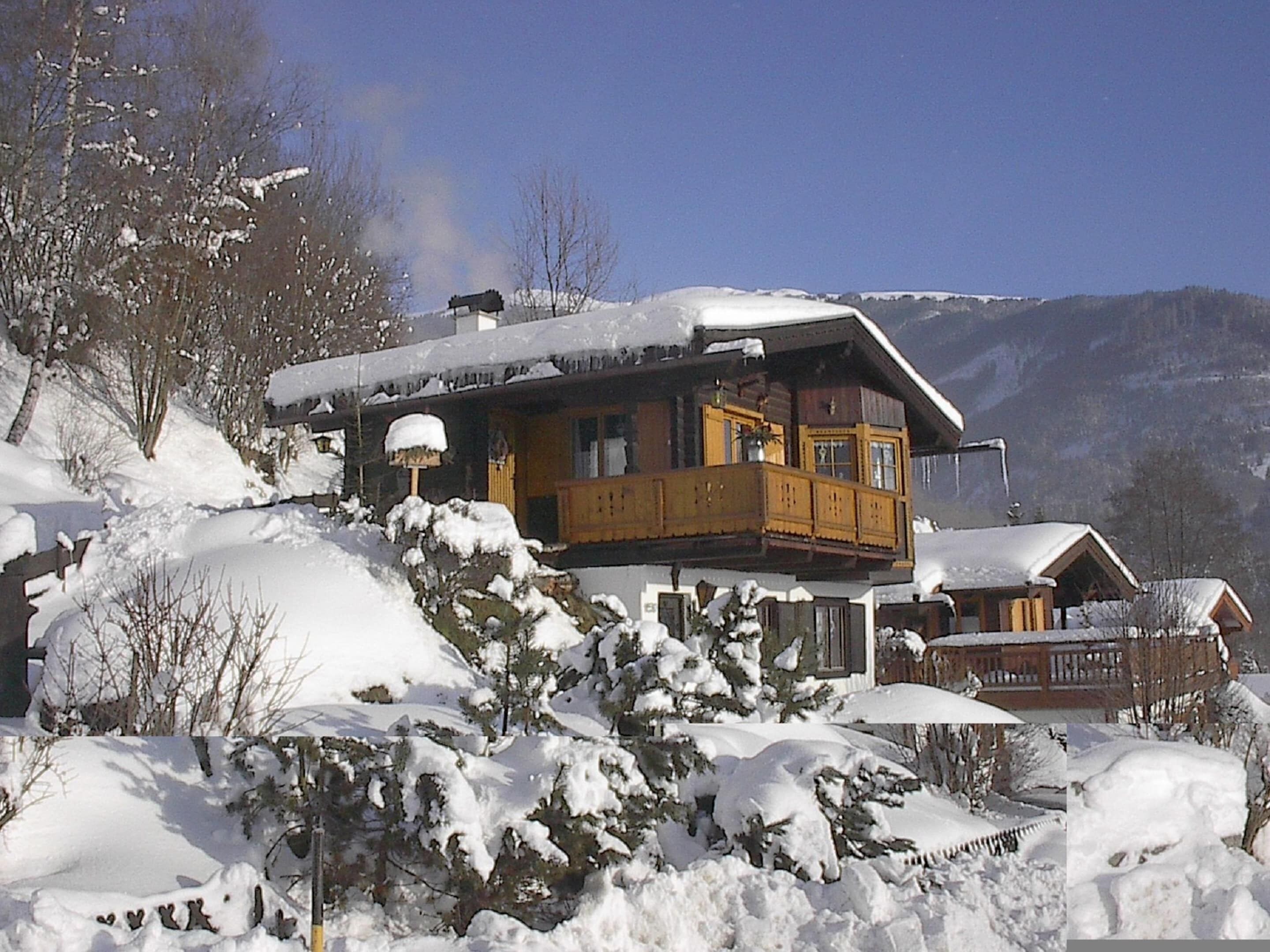 A chalet with a balcony, surrounded by snow-covered trees and mountains.