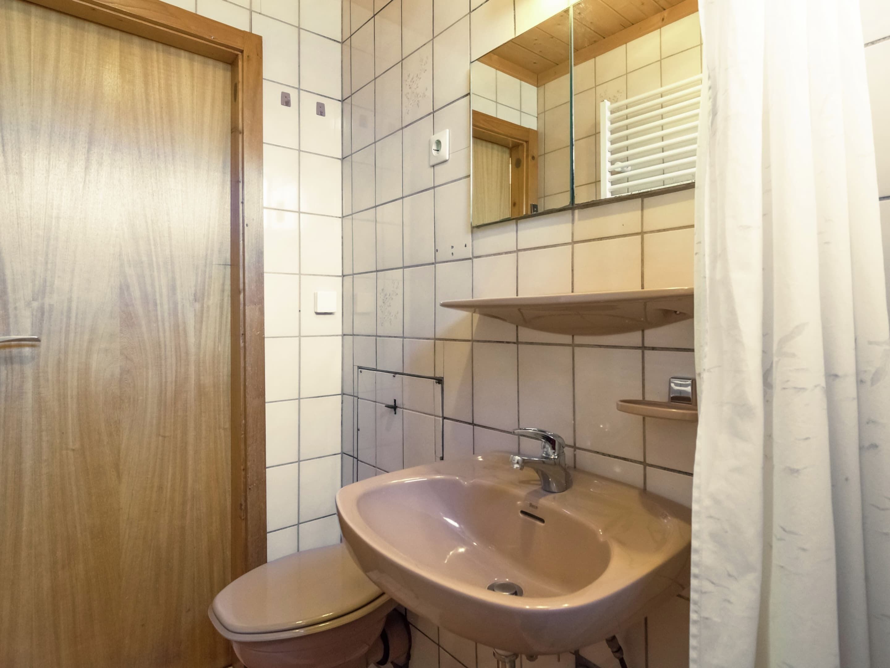 Une salle de bain équipée de toilettes, d’un lavabo, d’un miroir et de murs carrelés.