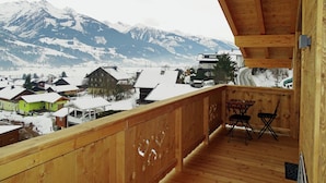 Un balcon en bois offrant une vue sur des maisons et des montagnes enneigées.
