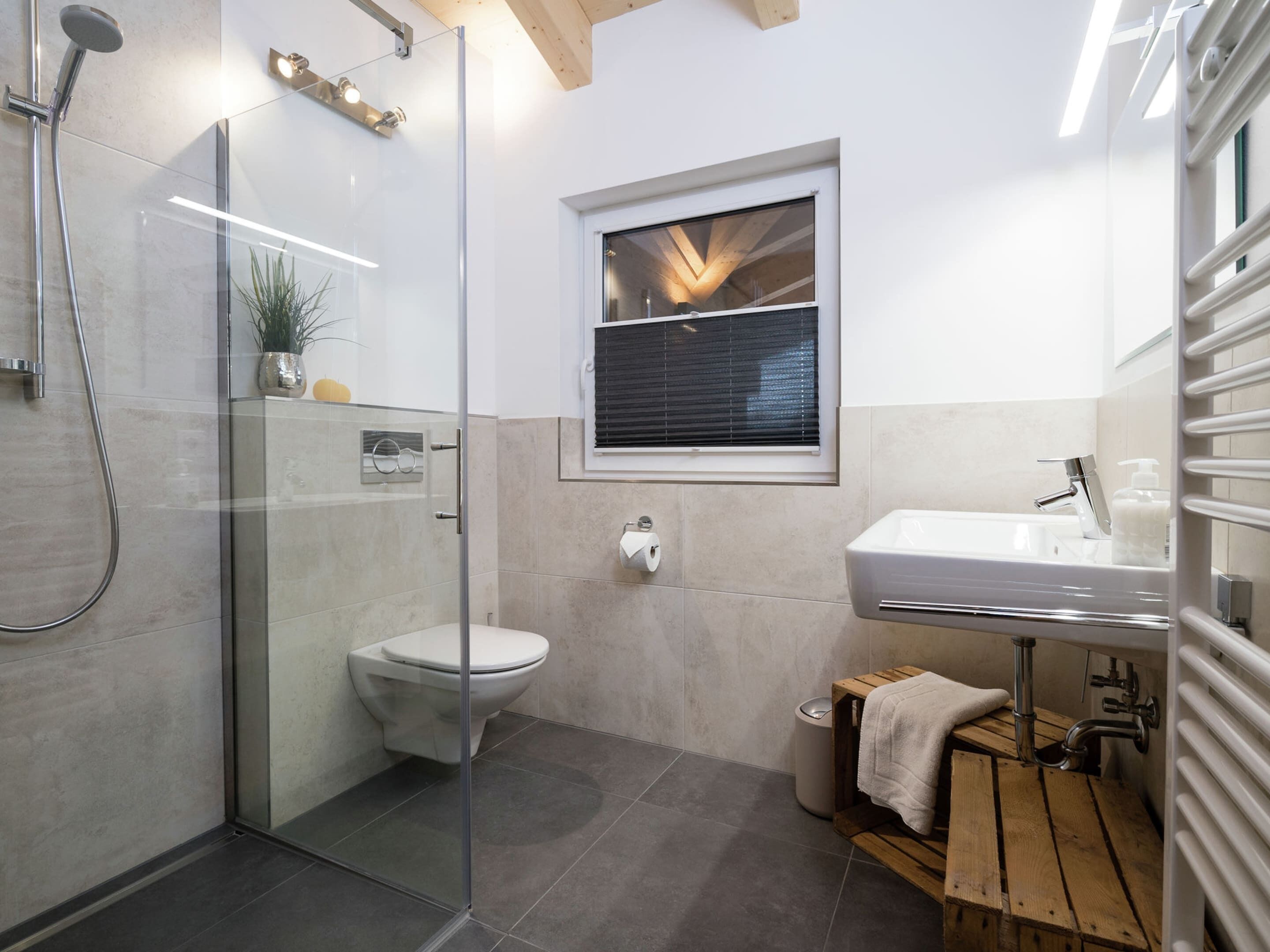 A modern bathroom with a glass-enclosed shower, a toilet, a sink, and a window with blinds.