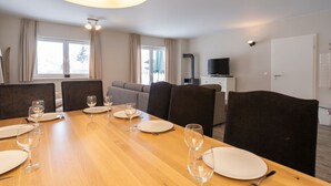 Un comedor con una mesa de madera preparada para cuatro personas, un sofá, un televisor y una ventana con cortinas.