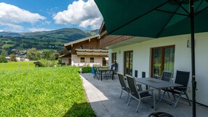 Un patio con mobiliario exterior, vistas a una cordillera y un edificio con toldo verde.