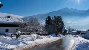 Een besneeuwde weg met huizen aan weerszijden, een heldere lucht en bergen op de achtergrond.