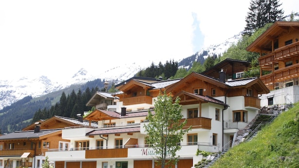 Un ensemble de bâtiments de style chalet en bois, dotés de balcons, se dressant sur un fond de montagnes enneigées.