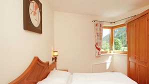 Une chambre avec un lit en bois, une table de chevet avec une lampe, une fenêtre avec des rideaux et une vue sur la verdure à l’extérieur.