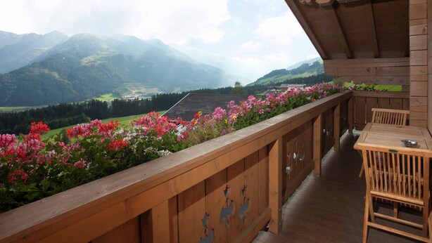 Un balcone in legno con vista sulle montagne e un giardino fiorito.