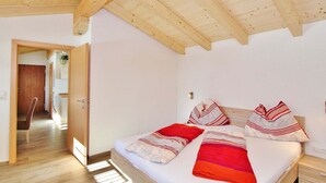 Una camera da letto con soffitto in legno, un letto con biancheria rossa e bianca e un comodino con un cassetto.