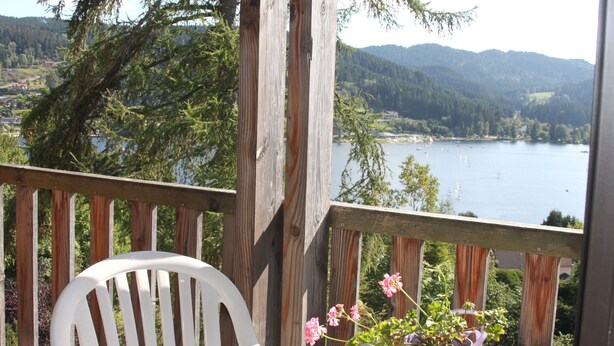 A wooden deck with a white chair and a table with a potted plant. - Air-conditioned apartment with stunning views of the lake and mountains. (Gérardmer, Grand Est)