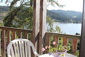 A wooden deck with a white chair and a table with a potted plant. - Air-conditioned apartment with stunning views of the lake and mountains. (Gérardmer, Grand Est)
