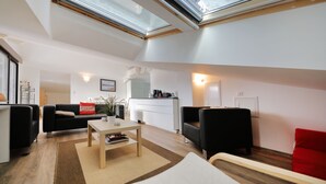 A modern living room with a sofa, a coffee table, and a red accent chair. There is a kitchen area in the background with a white countertop and a window above the sink. - Air-conditioned apartment with stunning views of the lake and mountains. (Gérardmer, Grand Est)