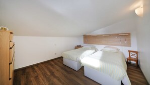A bedroom with two beds, wooden flooring, a wooden wardrobe, and a slanted ceiling. - Air-conditioned apartment with stunning views of the lake and mountains. (Gérardmer, Grand Est)