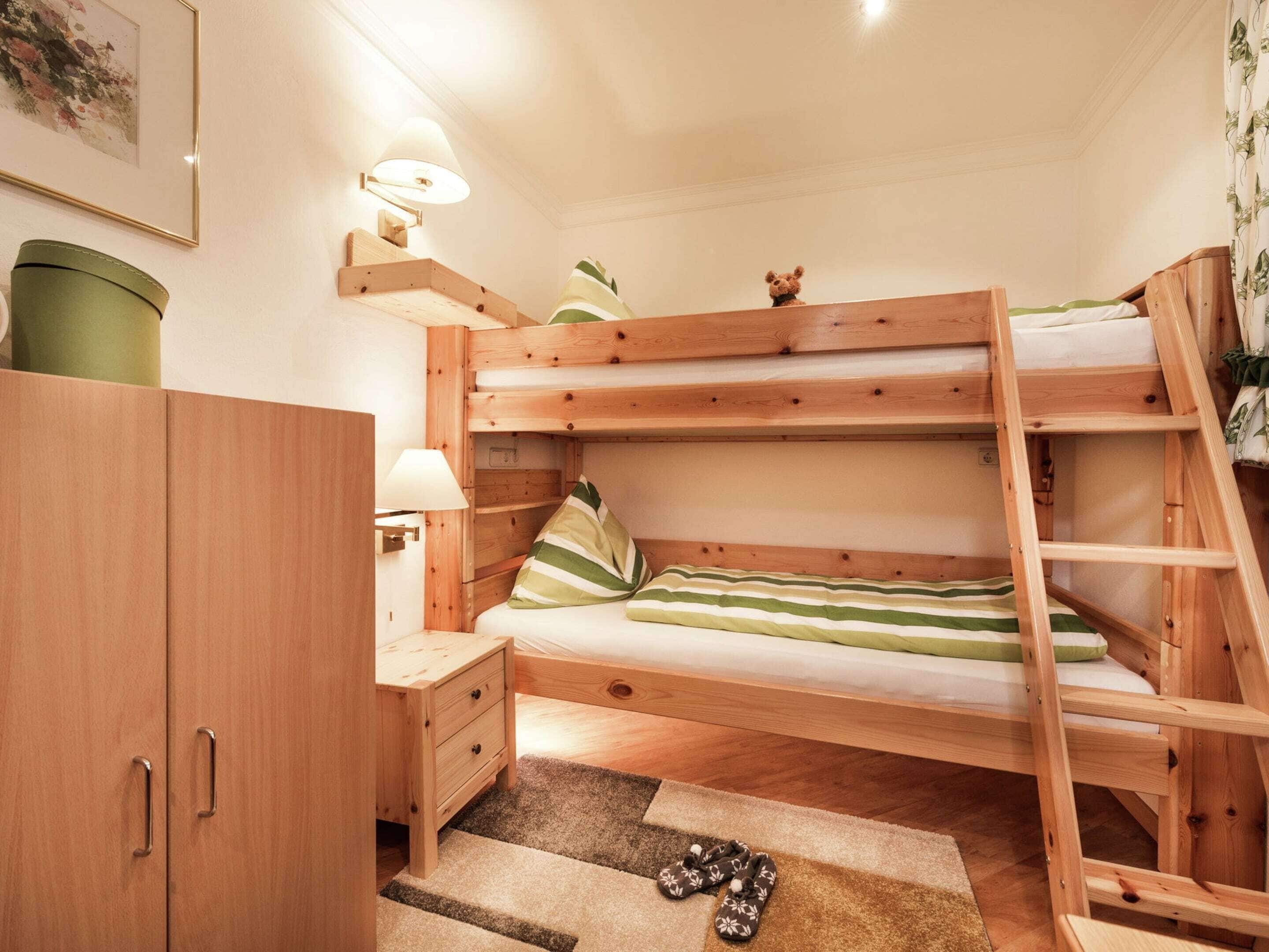 Una cama litera con escalera de madera, una mesita de noche, una lámpara y un pequeño armario.