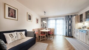 A modern living room with a dark blue sofa, a dining table with red chairs, and a kitchen area with wooden cabinets and a dishwasher. - Holiday Flat Gastein Near Ski Slopes (Bad Hofgastein)