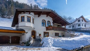 A two-story chalet with a balcony, a stone staircase, and a snow-covered driveway. - Holiday Flat Gastein Near Ski Slopes (Bad Hofgastein)