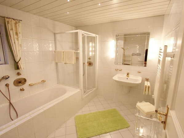A bathroom with a bathtub, shower, and sink, featuring white tiles and gold fixtures.