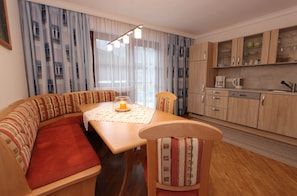 A cozy living area with a sofa, a dining table with a candle, and a kitchen with wooden cabinets and a coffee maker.