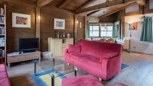 A cozy living room with wooden beams, a red sofa, a glass coffee table, and a TV on a wooden cabinet. - Spacious Apartment near Ski Area in Niedernsill (Niedernsill)