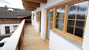 Ein schmaler Balkon mit Holzbalken, einer weißen Außenwand und großen Fenstern.