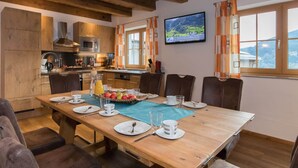 Ein Essbereich mit einem Holztisch, gedeckt für sechs Personen, eine Küche mit modernen Geräten und ein reizvoller Ausblick durch die Fenster.