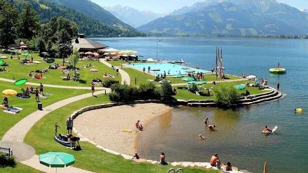 Ein Seehotel mit Schwimmbad, Liegestühlen und einer Rasenfläche mit Sonnenschirmen.