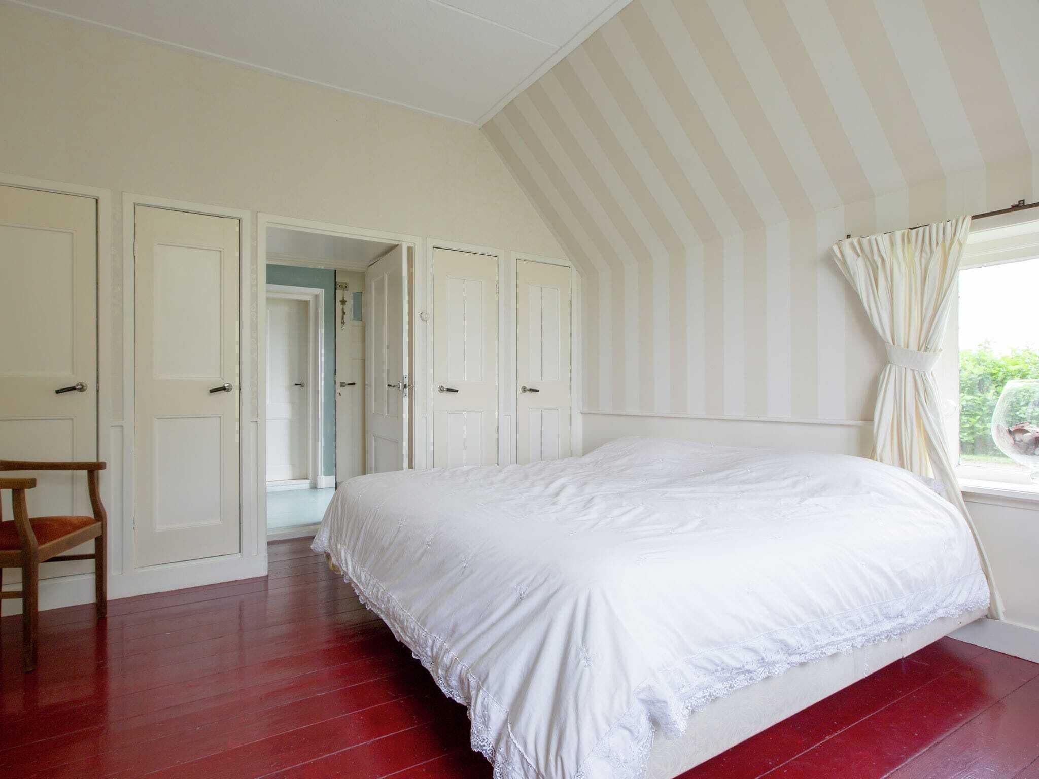 A bedroom with a large bed, a wooden chair, and a window with curtains.