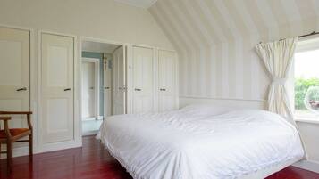 A bedroom with a large bed, a wooden chair, and a window with curtains.