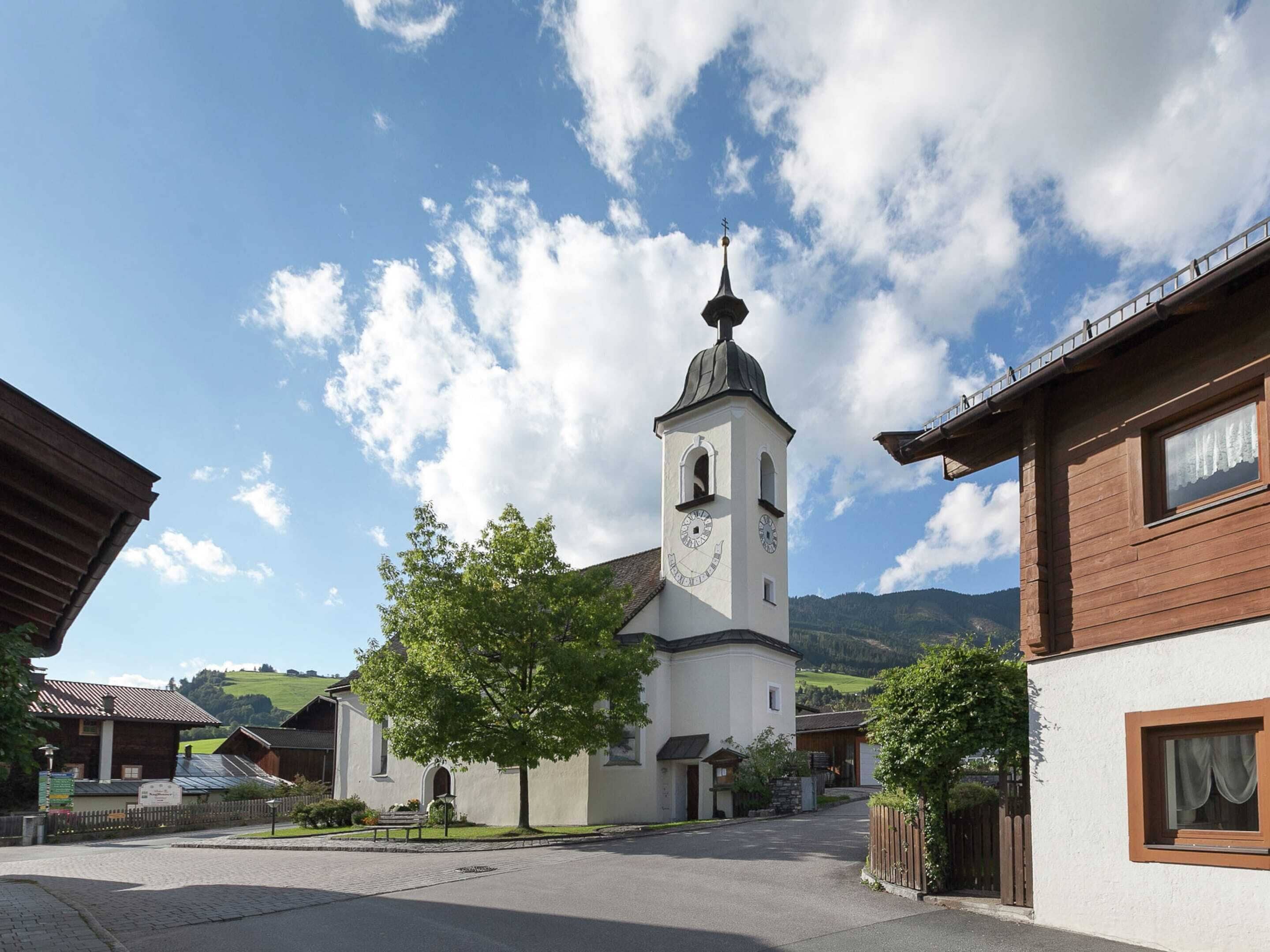 Une église dotée d’un clocher, entourée de bâtiments en bois et bordée d’une rue pavée.