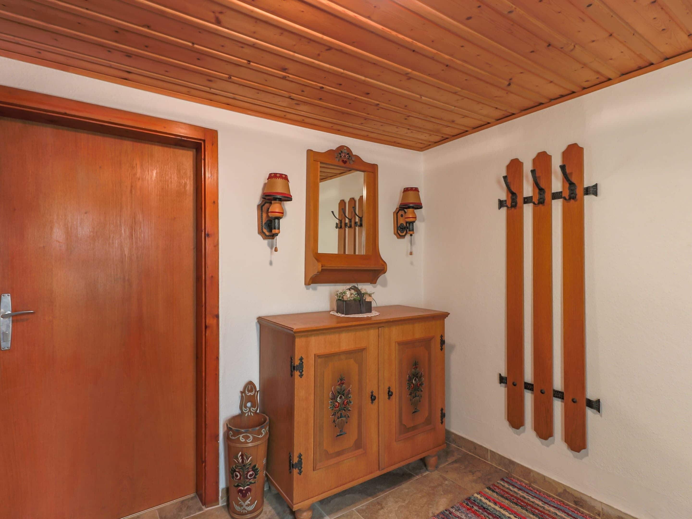 A wooden door, a wooden cabinet with a mirror, wall-mounted sconces, and a vertical wooden rack.
